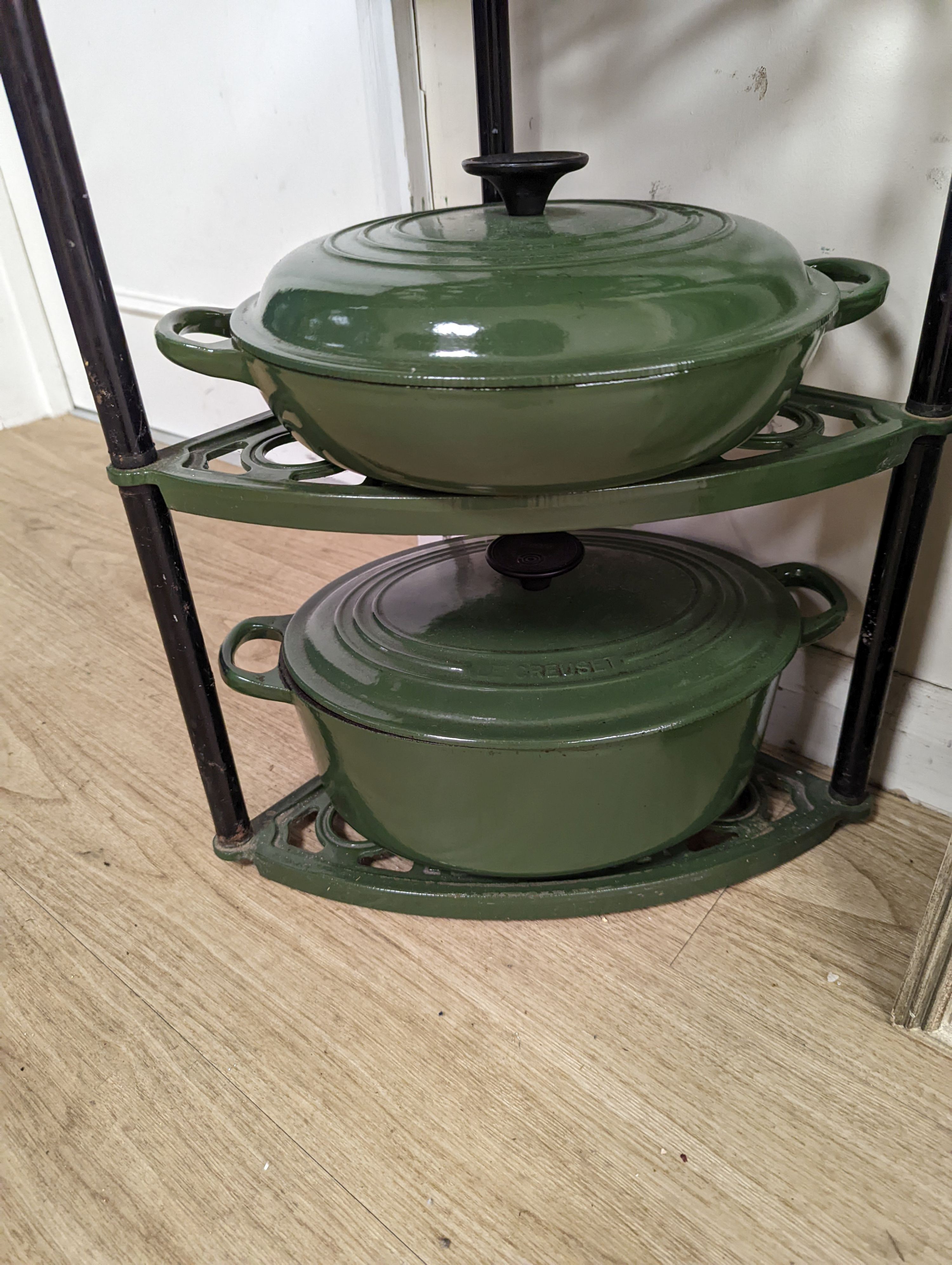 A green enamel Le Cruset pot stand, three pans and a bottle rack, stand 90 cms high.